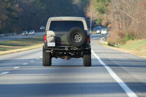 1982 Ford Bronco - A lifted Ford Bronco is seen from behind driving on a highway with other vehicles in the distance.