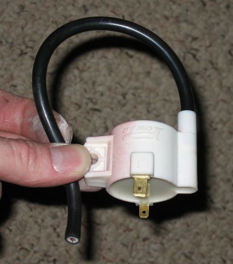 1900 Honda Big Red - A white ignition coil with a black wire is held by a hand. The part has brass connectors and visible text.