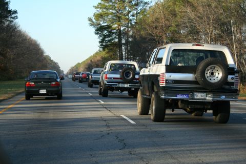 1982 Ford Bronco - A convoy of trucks and cars travels down a highway on a clear day.