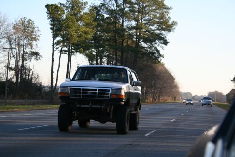 1982 Ford Bronco - A lifted silver SUV, likely a 1992 model, travels down a highway with other vehicles in the distance.
