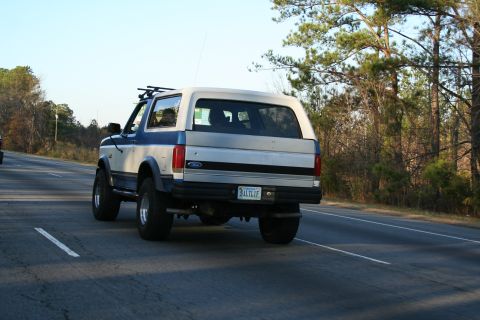 1982 Ford Bronco - This Ford Bronco is seen from behind on a paved road, with trees lining the side.
