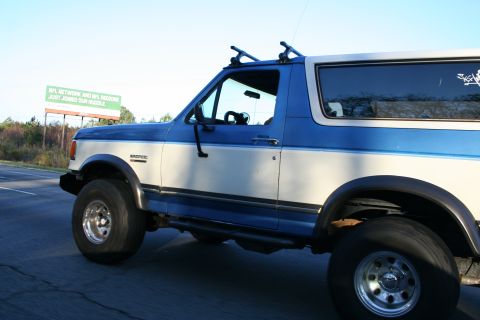 1982 Ford Bronco - This Ford Bronco is seen from the side, equipped with a roof rack and driving on a paved road.