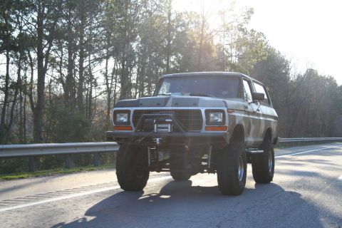 1982 Ford Bronco - This lifted Ford Bronco is driving down a highway with trees in the background.