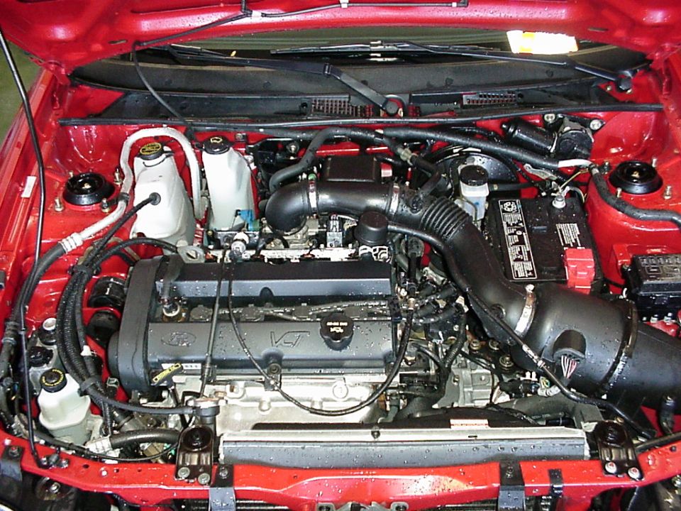 Engine bay of a red Ford showing 4-cylinder engine, air intake, battery and reservoirs