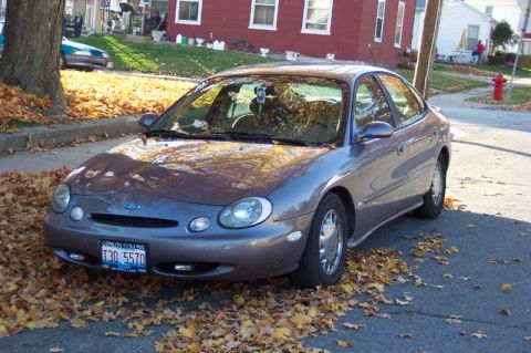 1996 Ford Taurus - A gray Ford Taurus is parked on a street, surrounded by fallen leaves during autumn.