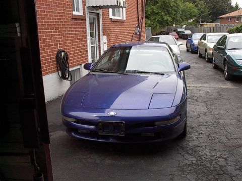 1993 Ford Probe - A blue 1993 Ford Probe is parked in front of a brick building with other vehicles lined up behind it.