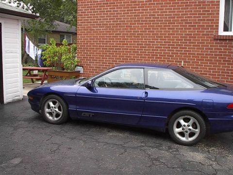 1993 Ford Probe - A blue coupe is parked in a driveway with a brick building in the background.