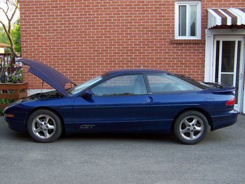 1993 Ford Probe - A blue 1993 Ford Probe GT coupe is parked in front of a brick building with its hood open.