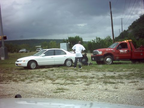 1996 Ford Bronco - A white sedan is parked next to a red tow truck on the side of the road under a cloudy sky.