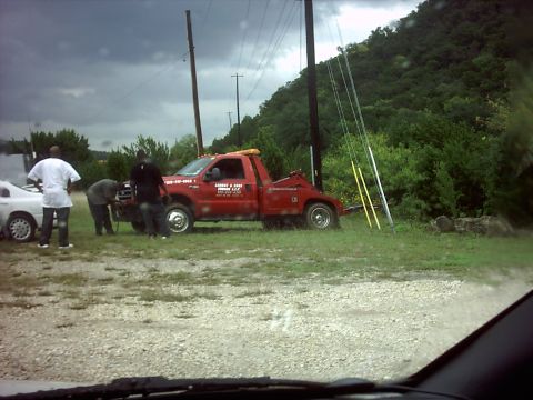 1996 Ford Bronco - A tow truck is loading a white car. The tow truck has text on its door.