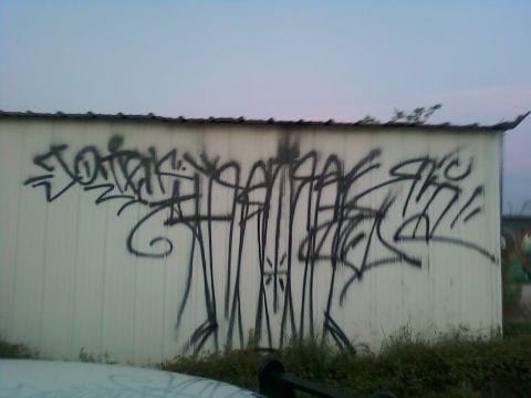 1996 Ford Bronco - Graffiti covers the side of a white building, with a portion of a vehicle visible at the bottom of the frame.