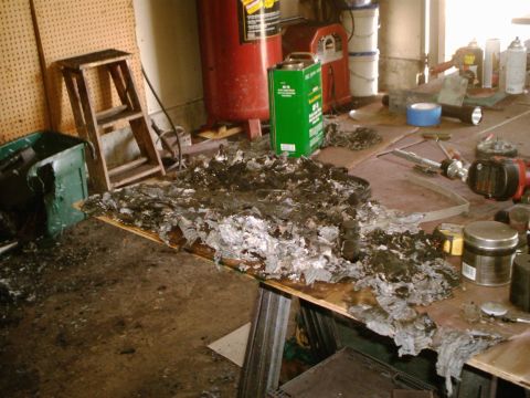 1989 Ford Bronco - The aftermath of a fire is seen on a workbench in a garage, with tools and equipment scattered around.