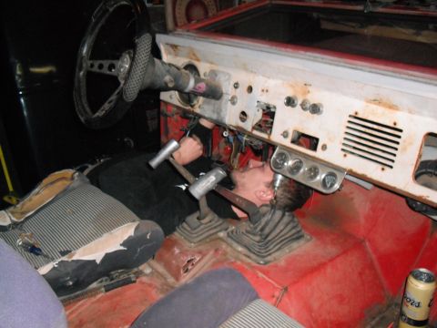 1968 Ford Bronco - A person is working on the wiring under the dashboard of a vehicle, with the steering wheel and seats visible.