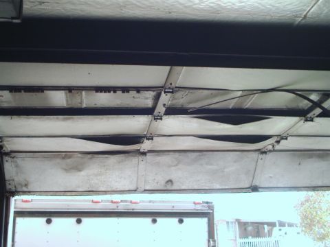 1989 Ford Bronco - The interior of a garage door shows damage to its panels, with a trailer visible beneath it.