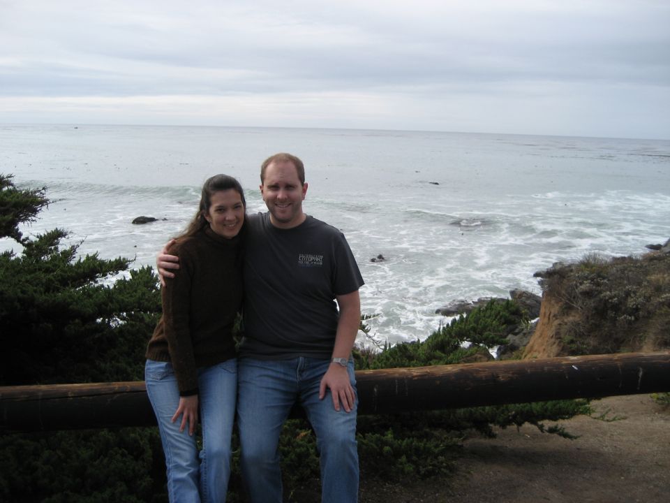 Couple posing for a photo by the ocean with a wooden railing in the foreground