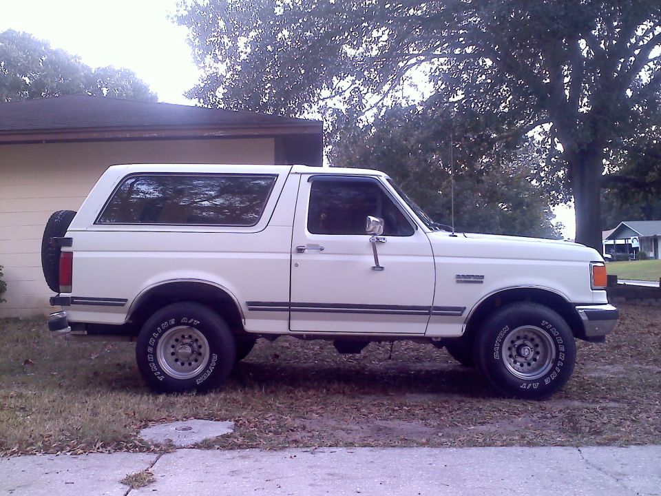 White 1987 Ford Bronco SUV parked on grass, side view, with spare tire on rear door