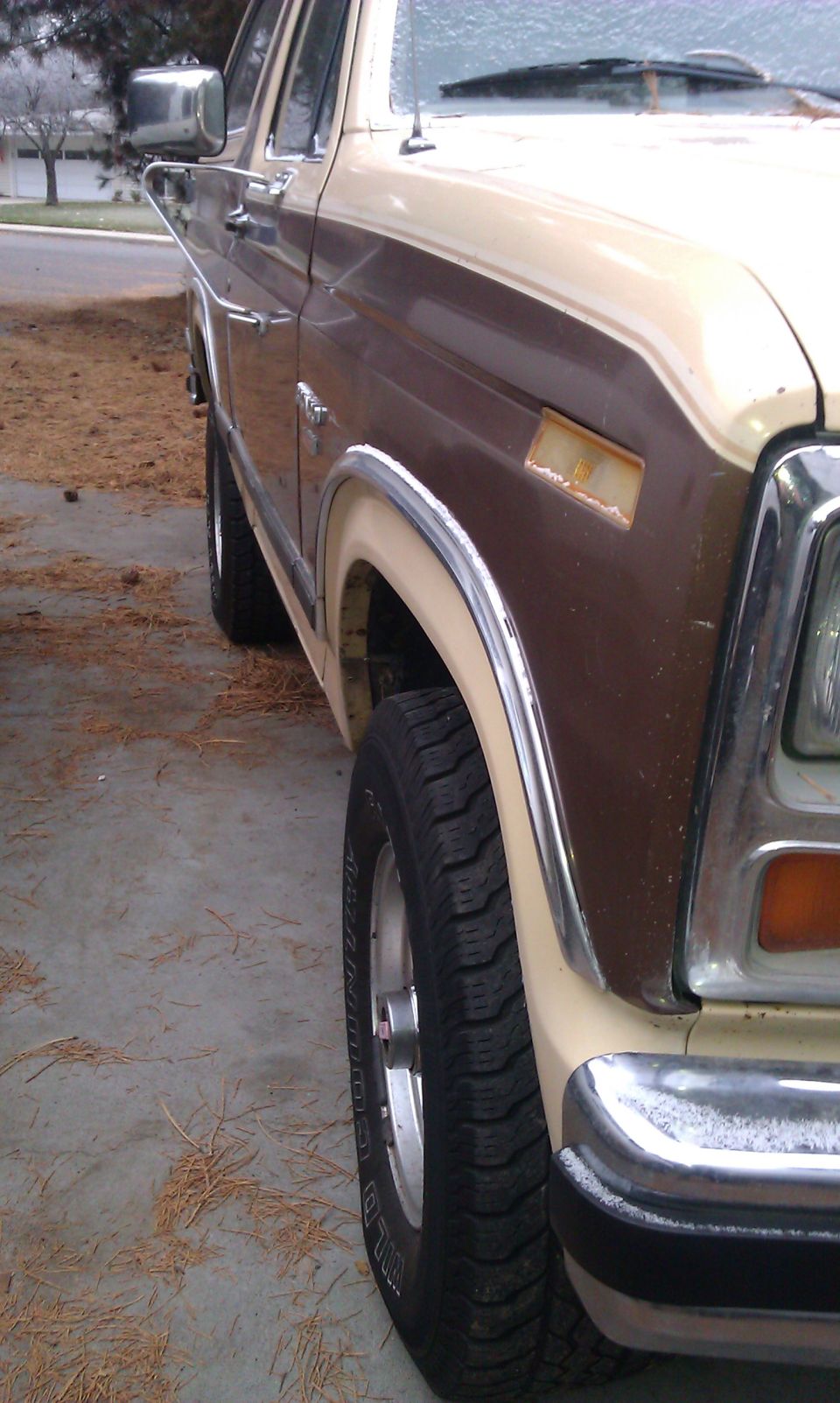 Close-up of 1980s Ford Bronco front fender, wheel, and chrome trim. Two-tone brown and tan paint
