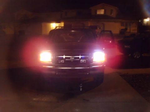 1996 Ford Bronco - Front view of a dark Ford Bronco at night, with headlights illuminated. A second vehicle is visible to the right.