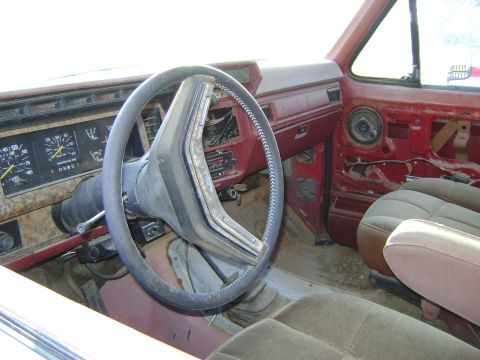 1968 Ford Mustang - Interior of a red truck, showing the dashboard, steering wheel, and seats. The door panel is removed.