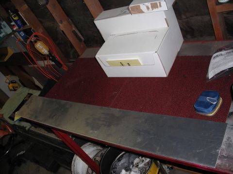1968 Ford Bronco - A long blank strip of aluminum sheet, uncut raw stock for a fabricated dash panel, lies across a red carpeted workbench in a garage next to…