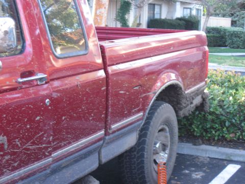 1995 Ford F-150 - This red 1995 Ford F-150 shows signs of off-road use, with mud caked on its tires and lower body panels.
