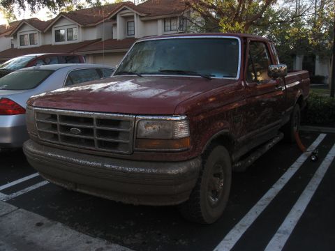 1995 Ford F-150 - Mud-covered 1995 Ford F-150 pickup truck parked in a lot next to another vehicle.