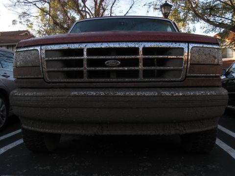 1995 Ford F-150 - The front of a dirty 1995 Ford F-150 pickup truck is covered in mud, obscuring some of its details.