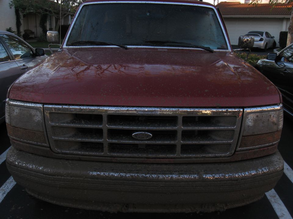 1995 Ford F-150 front view, covered in dirt and dust. Grille and bumper are heavily soiled