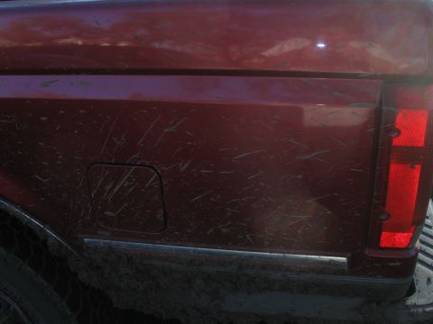 1995 Ford F-150 - The rear quarter panel of a dirty red pickup truck shows a fuel door and part of the taillight assembly.