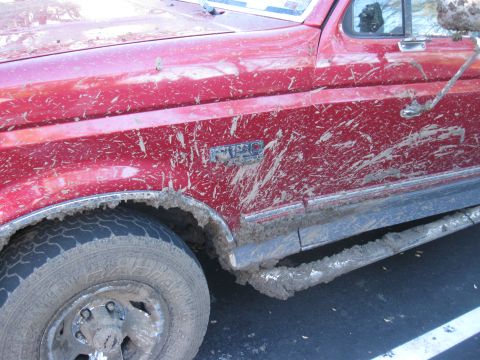 1995 Ford F-150 - This red 1995 Ford F-150 shows significant mud splatter, indicating recent off-road use.