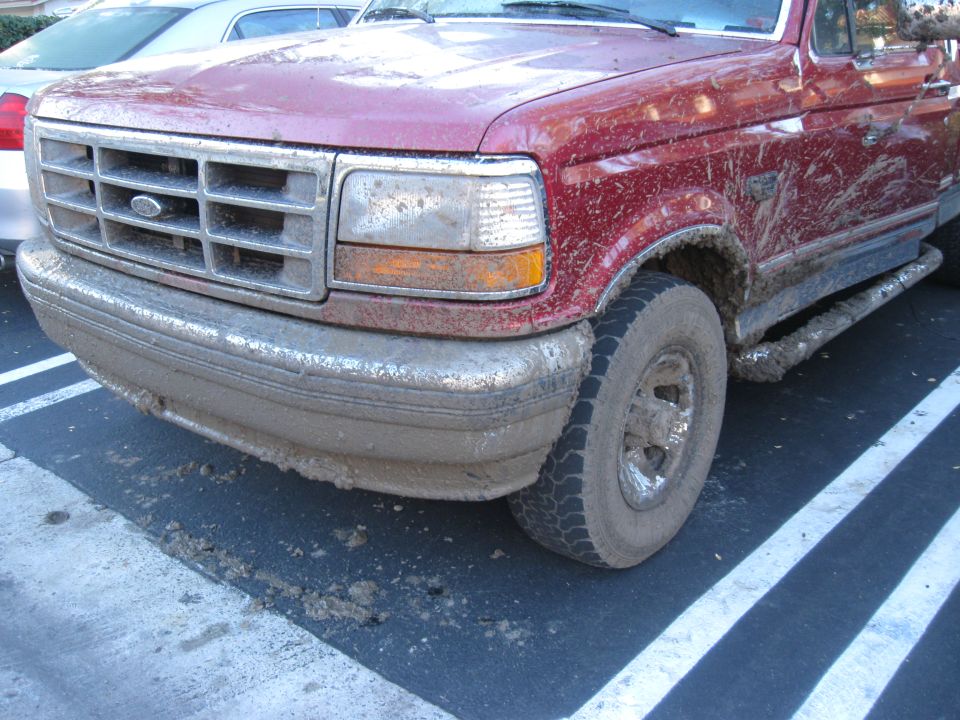 Mud-splattered red 1995 Ford F-150 front quarter panel and tire