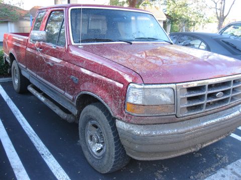 1995 Ford F-150 - Mud-splattered red pickup truck parked in a lot, showing its front and side.