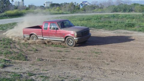 1995 Ford F-150 - A red pickup truck drifts on a dirt road, kicking up a cloud of dust.