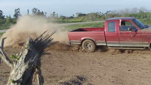 1995 Ford F-150 - Red 1995 Ford F-150 powers through dirt, sending up a plume of dust.