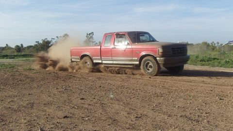 1995 Ford F-150 - A red pickup truck drives off-road, kicking up a cloud of dust.