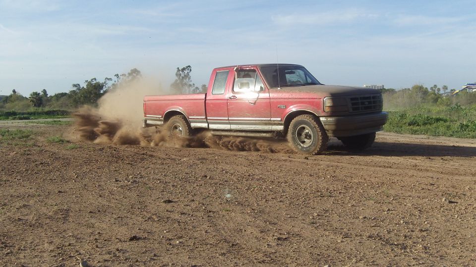 Red pickup truck kicking up dust while driving on a dirt road