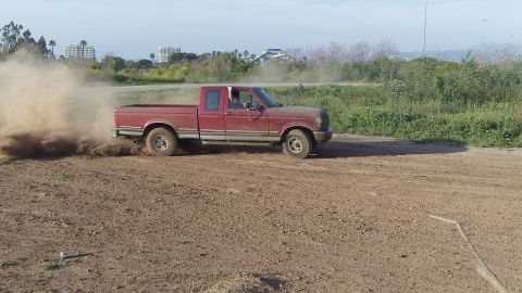 1995 Ford F-150 - A red 1995 Ford F-150 is seen drifting on a dirt track, creating a cloud of dust.