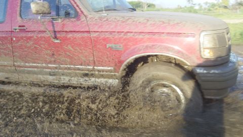 1995 Ford F-150 - This 1995 Ford F-150 is navigating a muddy off-road trail, kicking up dirt and water.