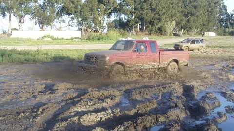 1995 Ford F-150 - A red pickup truck navigates a muddy track, with another vehicle visible in the background.