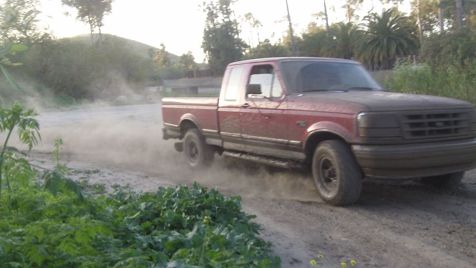 Red 1995 Ford F-150 driving on dirt road