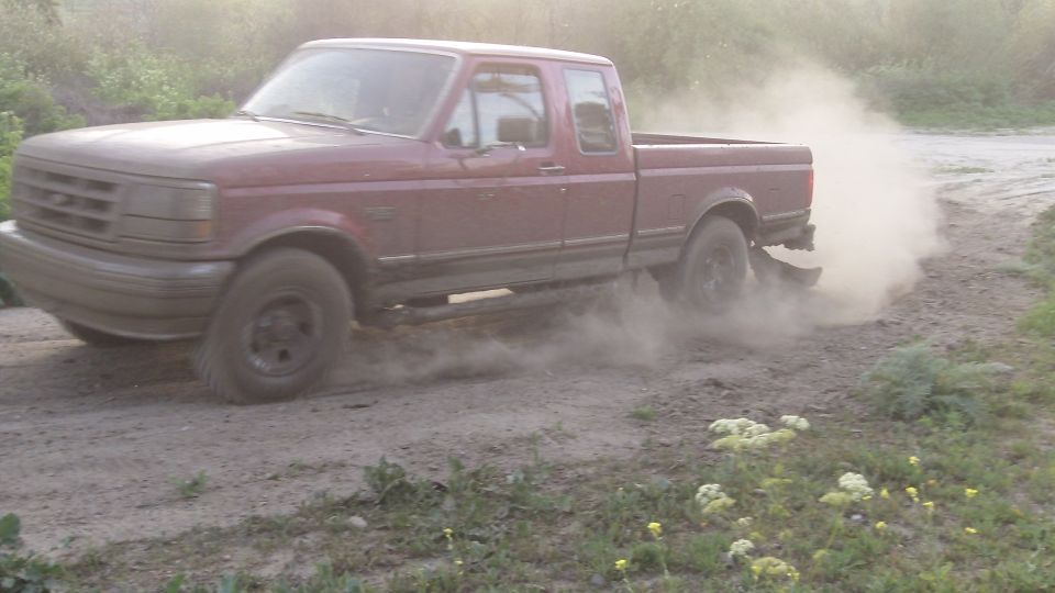 red pickup truck kicking up dust on a dirt road