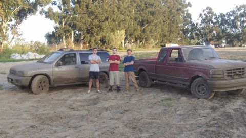 1995 Ford F-150 - Three young men stand with two muddy vehicles, a Ford F-150 pickup and an SUV, in an outdoor setting.
