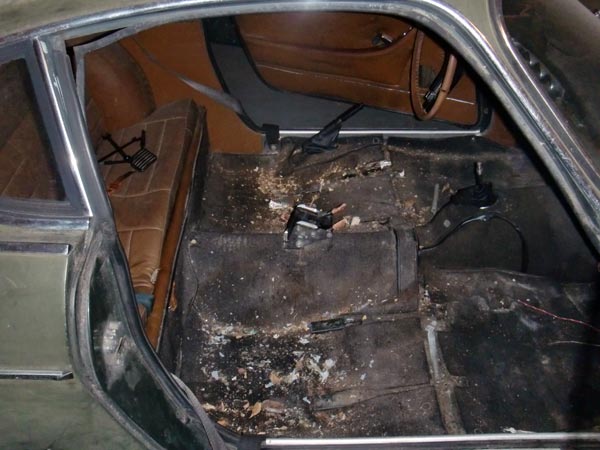 Dirty stripped coupe interior with tan seats and exposed shifter, viewed through open door