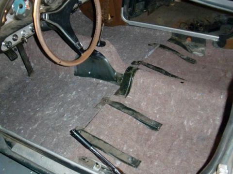 1969 Volvo P1800 - The interior of a car is shown with the floor carpet removed, revealing the pedals and steering wheel.