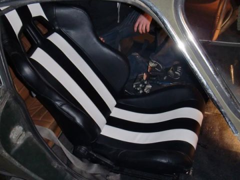1969 Volvo P1800 - The interior of a car features racing seats with bold black and white stripes, and a person's legs are visible in the driver's seat.