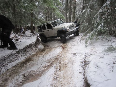 2008 Jeep Wrangler - A Jeep Wrangler navigates a challenging snowy and muddy path in a wooded area.
