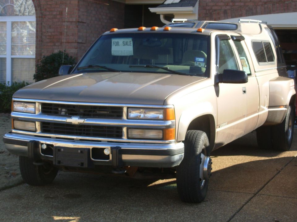 Tan Chevrolet crew-cab dually pickup with For Sale sign in driveway