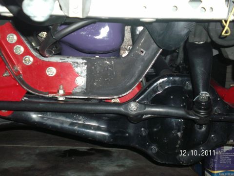 1996 Ford Bronco - Underside view of a solid front axle with black differential housing, showing the tie rod running above the axle tube and a tie rod end wit…