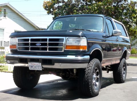 1995 Ford Bronco - This lifted Ford Bronco is shown from the front three-quarter view, highlighting its off-road tires and chrome accents.