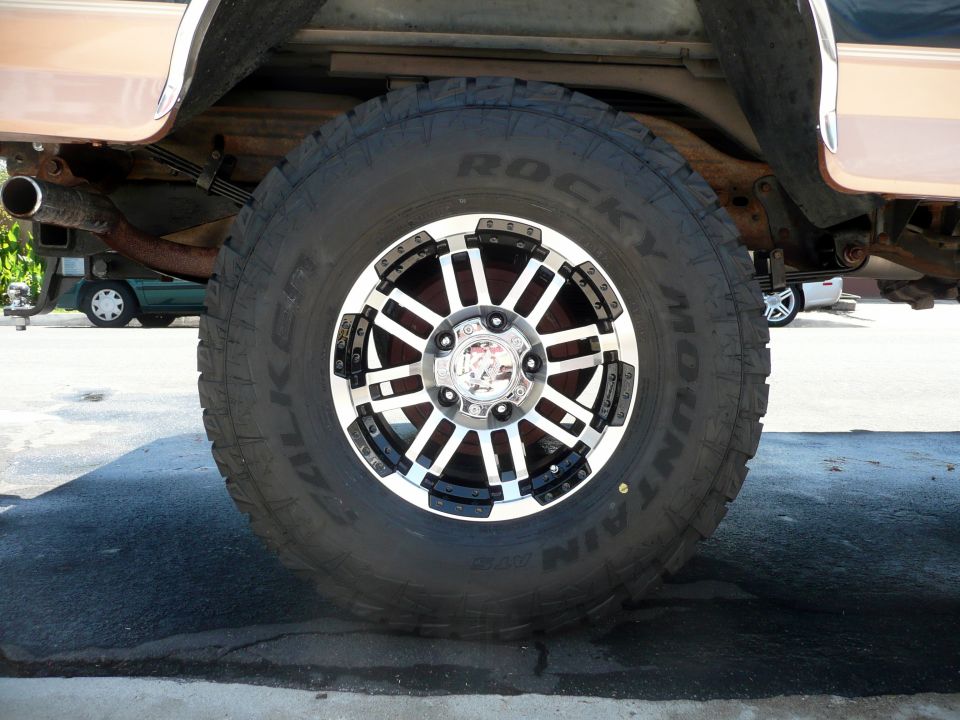1995 Ford Bronco rear wheel with aftermarket chrome and black rim, Rocky Mountain All Terrain tires, and visible exhaust pipe